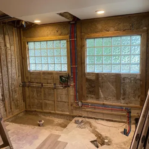 A bathroom under construction with a lot of pipes and windows.