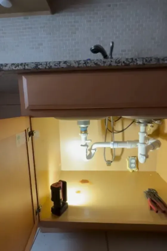 Open sink cabinet showing newly installed white PVC drain pipes and P-trap under a granite countertop